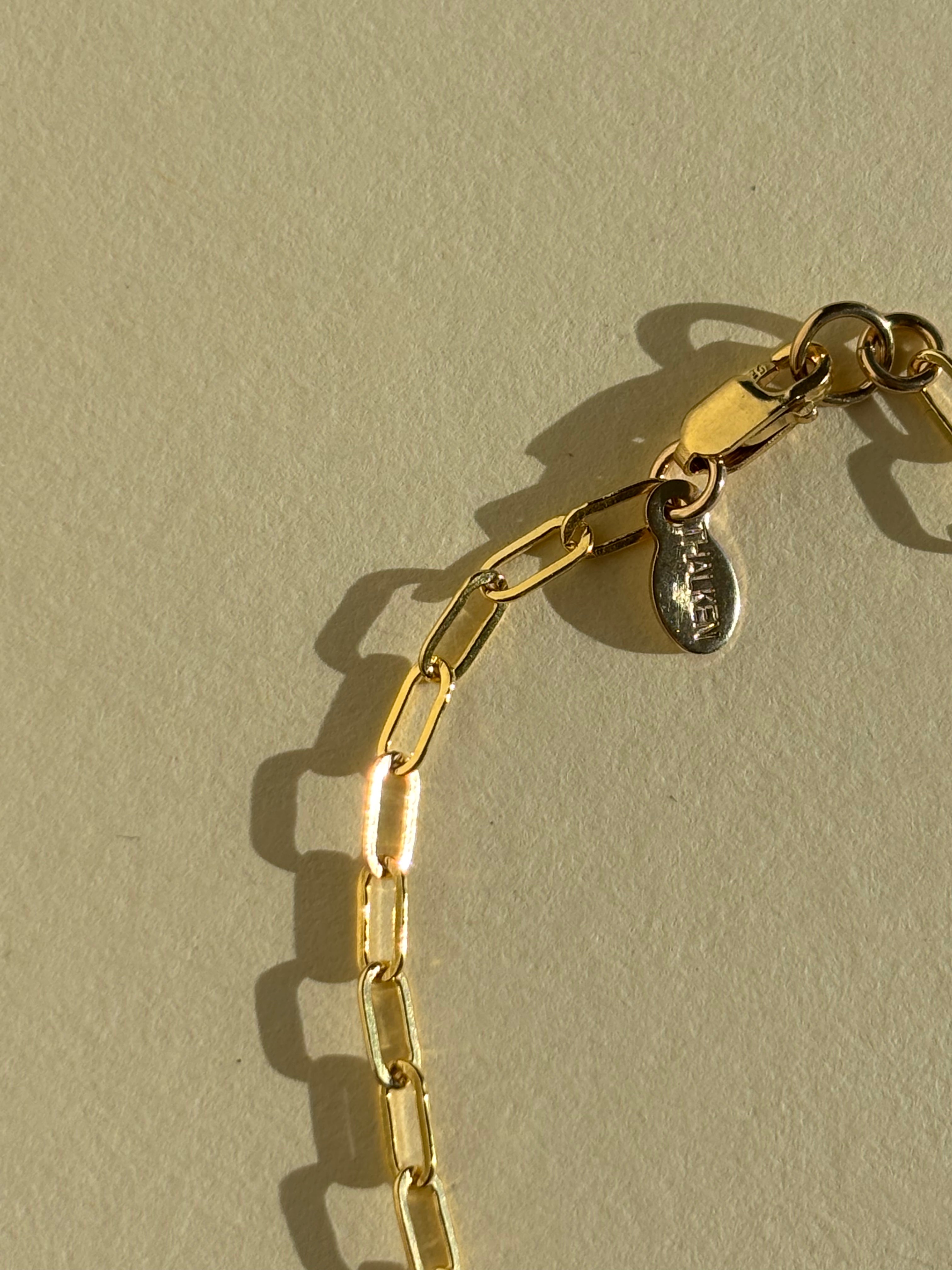 Close-up of metal THALKEN tag detail of Thalken's small link paperclip necklace