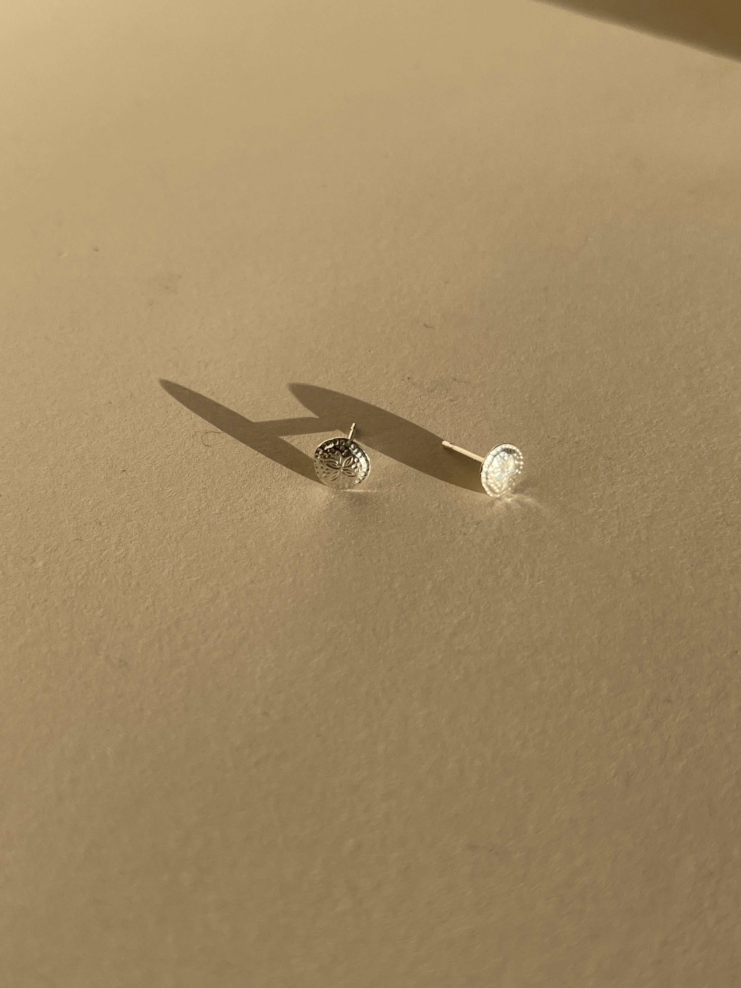 Pair of small sterling silver sand dollar studs on a neutral background