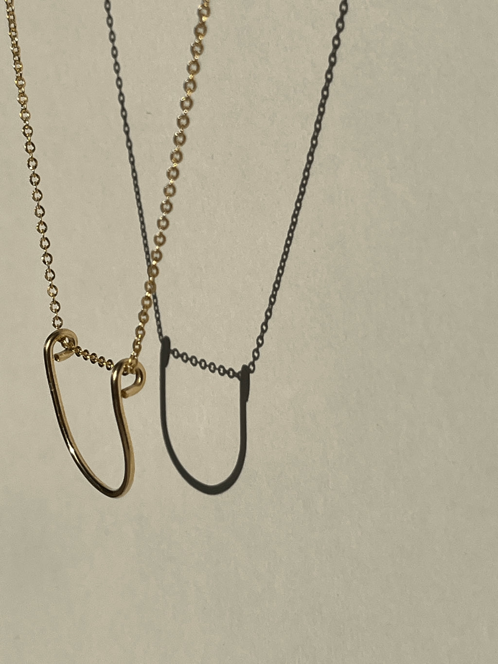 Yellow gold-filled U-shaped pendant necklace suspended in the air, close-up view.