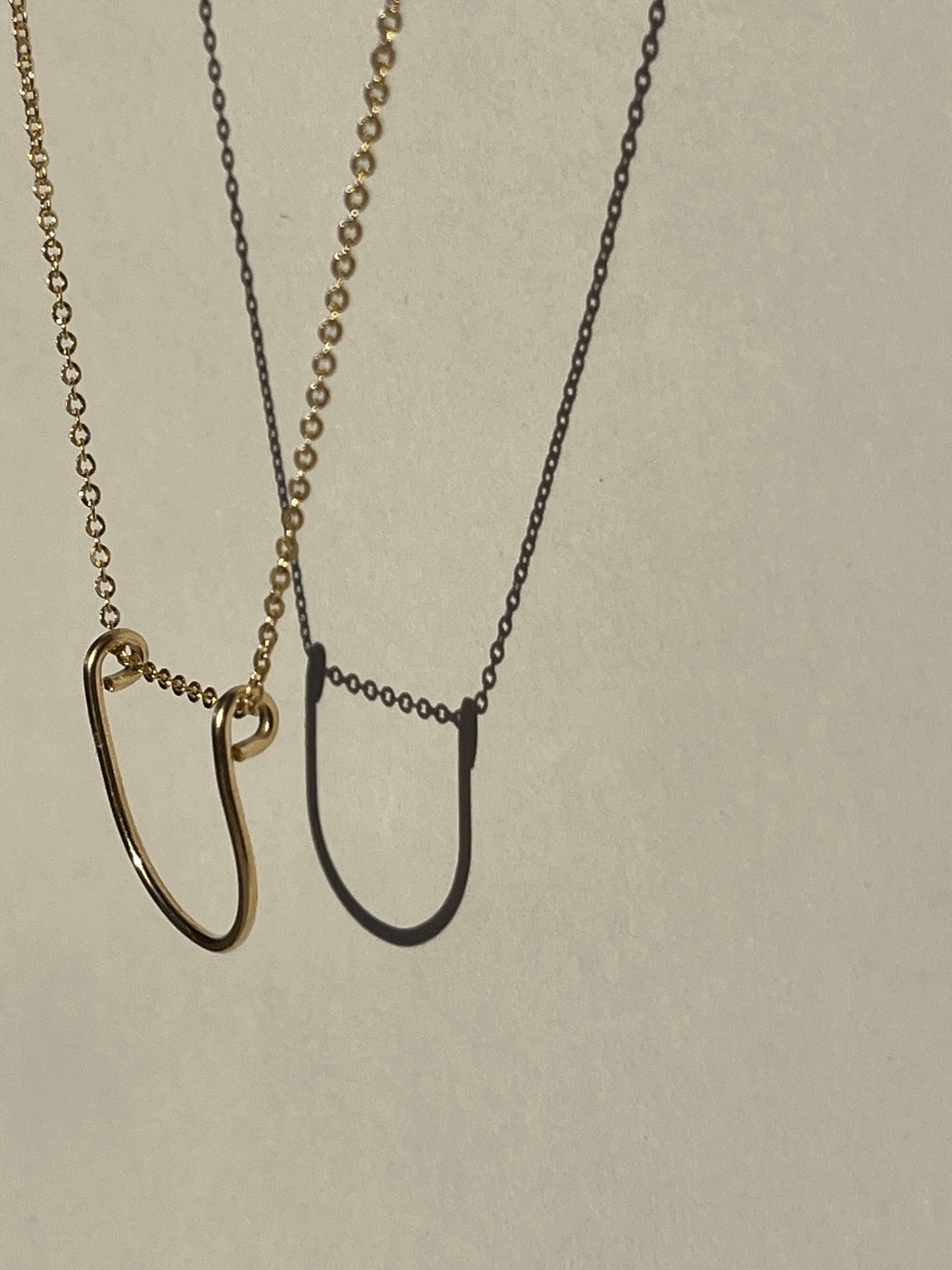 Yellow gold-filled U-shaped pendant necklace suspended in the air, close-up view.