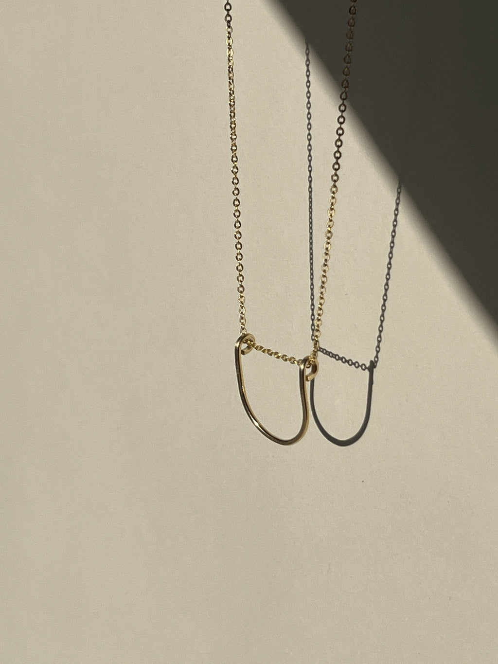 ellow gold-filled U-shaped pendant necklace suspended in the air, angled perspective