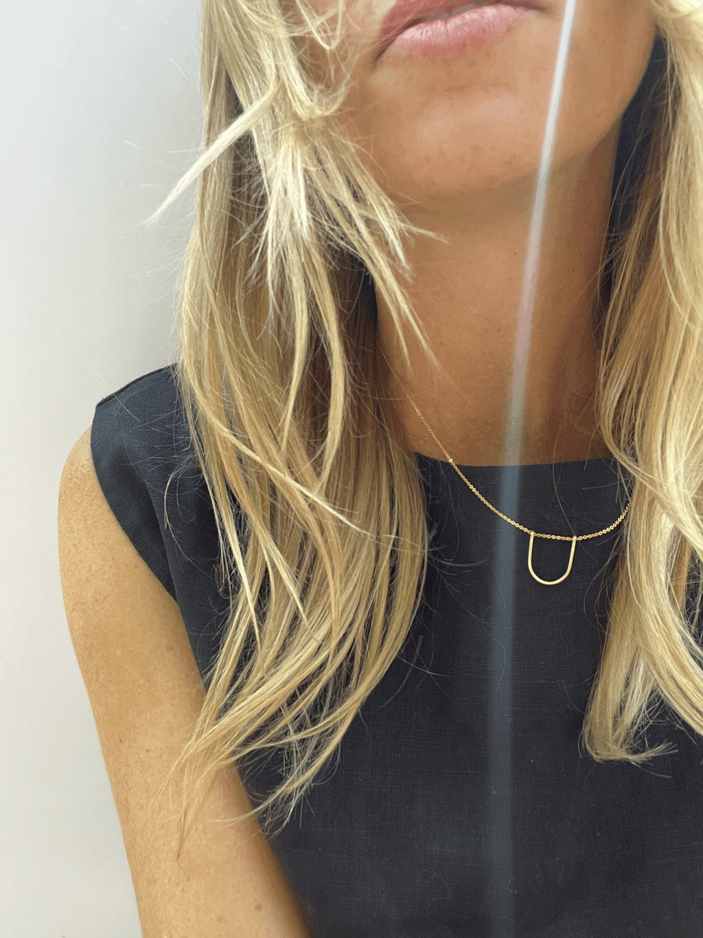 Model with blond hair wearing the yellow gold-filled U-shaped pendant necklace with a black linen top