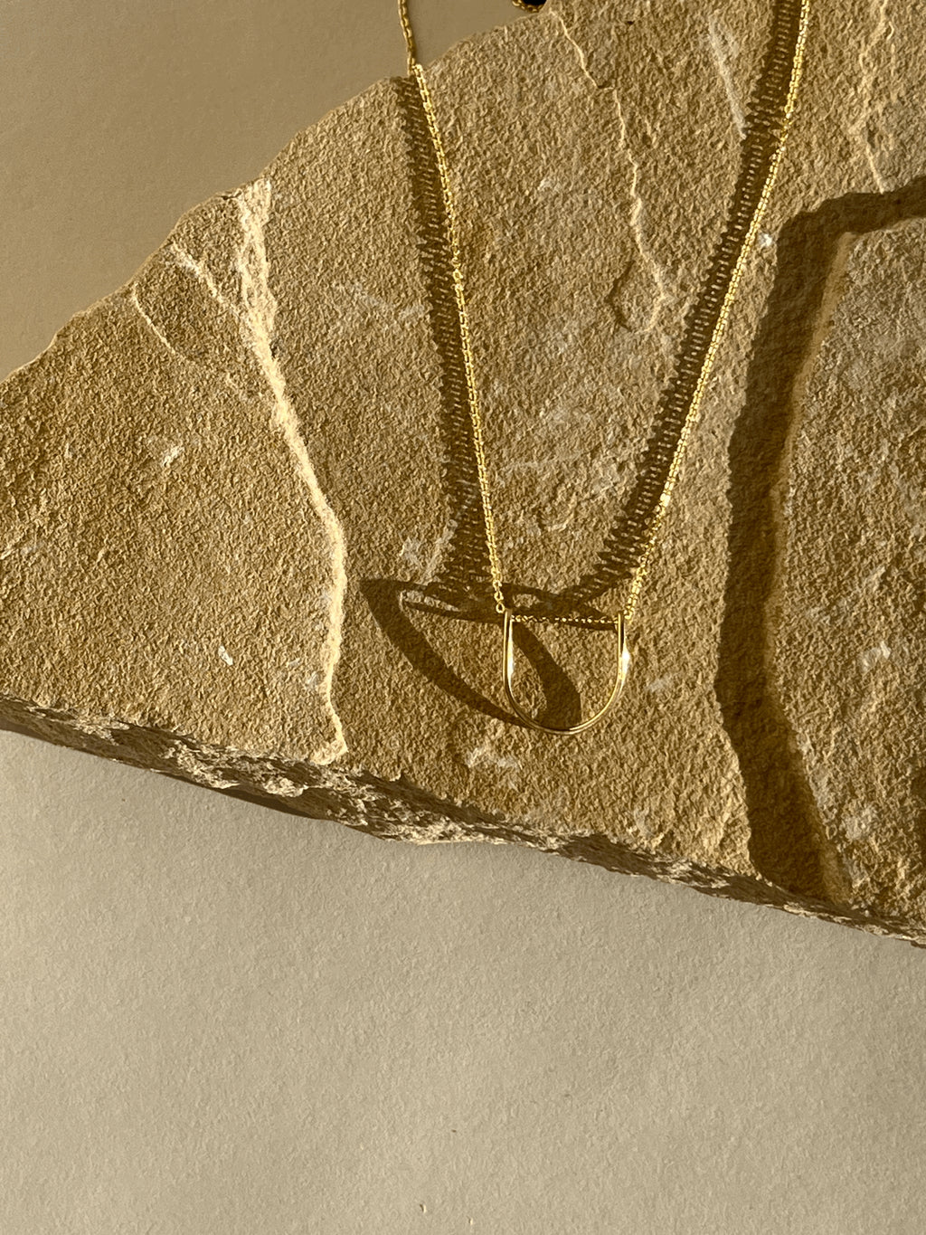Yellow gold-filled U-shaped pendant necklace displayed on a rock with warm lighting