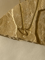 Yellow gold-filled U-shaped pendant necklace displayed on a rock with warm lighting