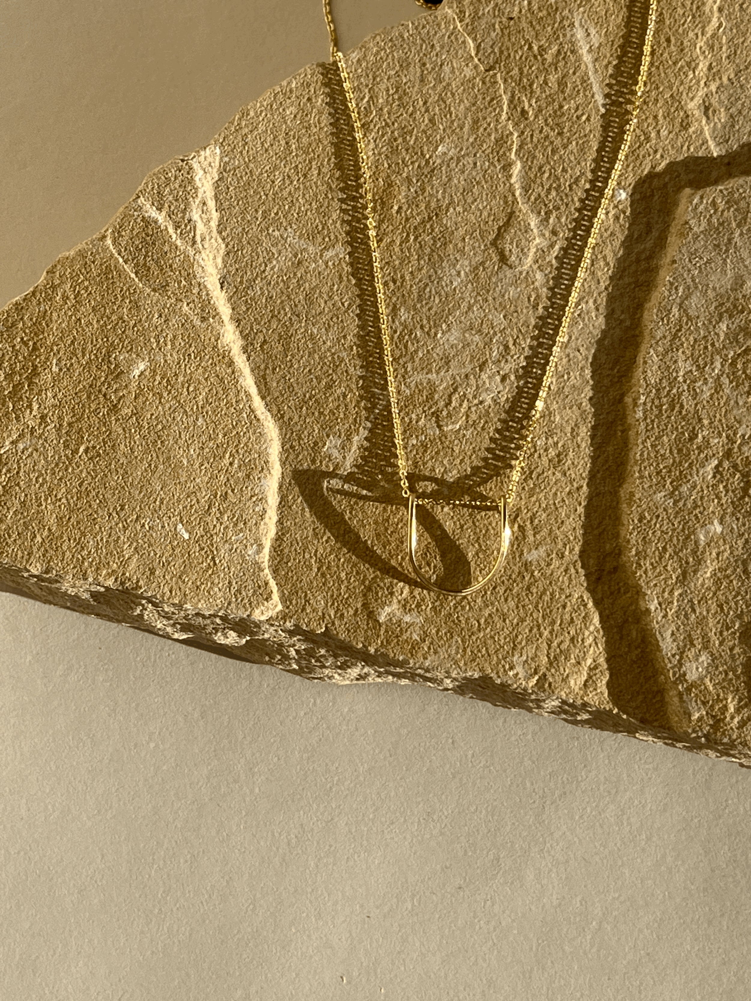 Yellow gold-filled U-shaped pendant necklace displayed on a rock with warm lighting