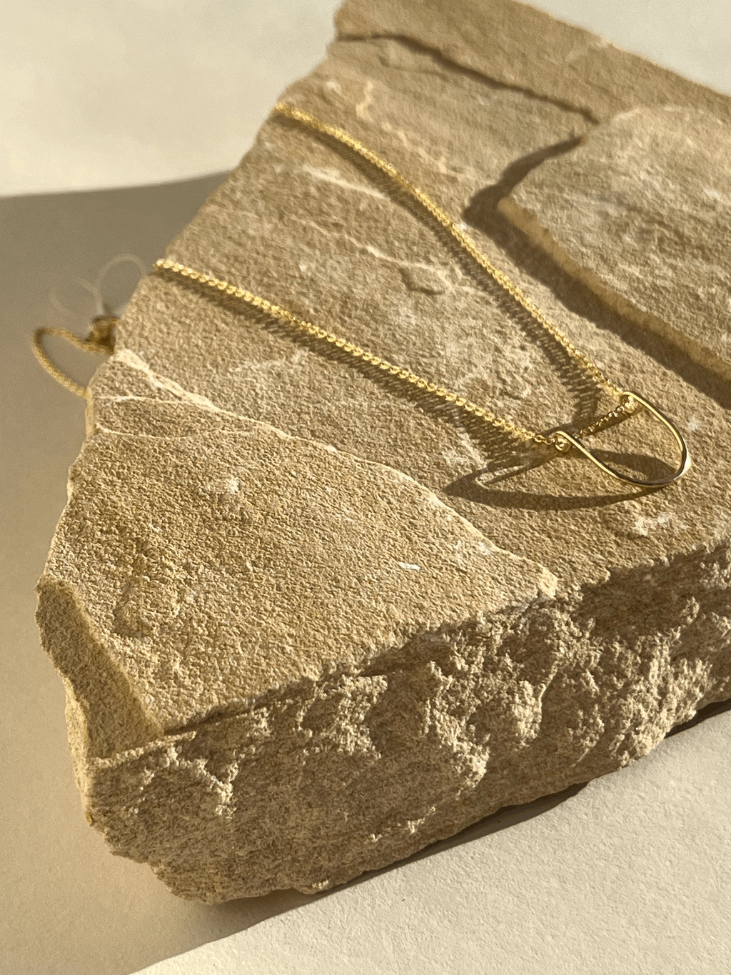 Yellow gold-filled U-shaped pendant necklace draped on a rock, glowing in extra warm lighting