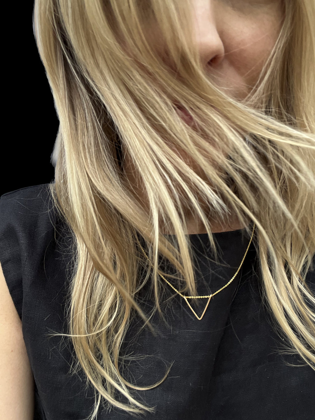 Model wearing yellow gold-filled V necklace over a black linen shirt, hair flowing loosely across face
