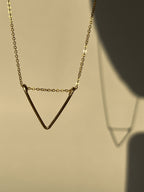 Yellow gold-filled V pendant necklace suspended in air, casting soft shadows against a neutral backdrop