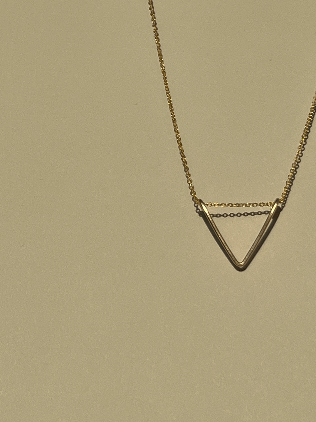 Close-up shot of yellow gold-filled V pendant necklace suspended in air against a warm neutral backdrop