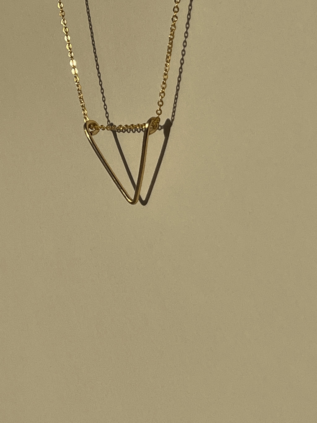 Side view of yellow gold-filled V pendant necklace suspended in air with shadows on a neutral background