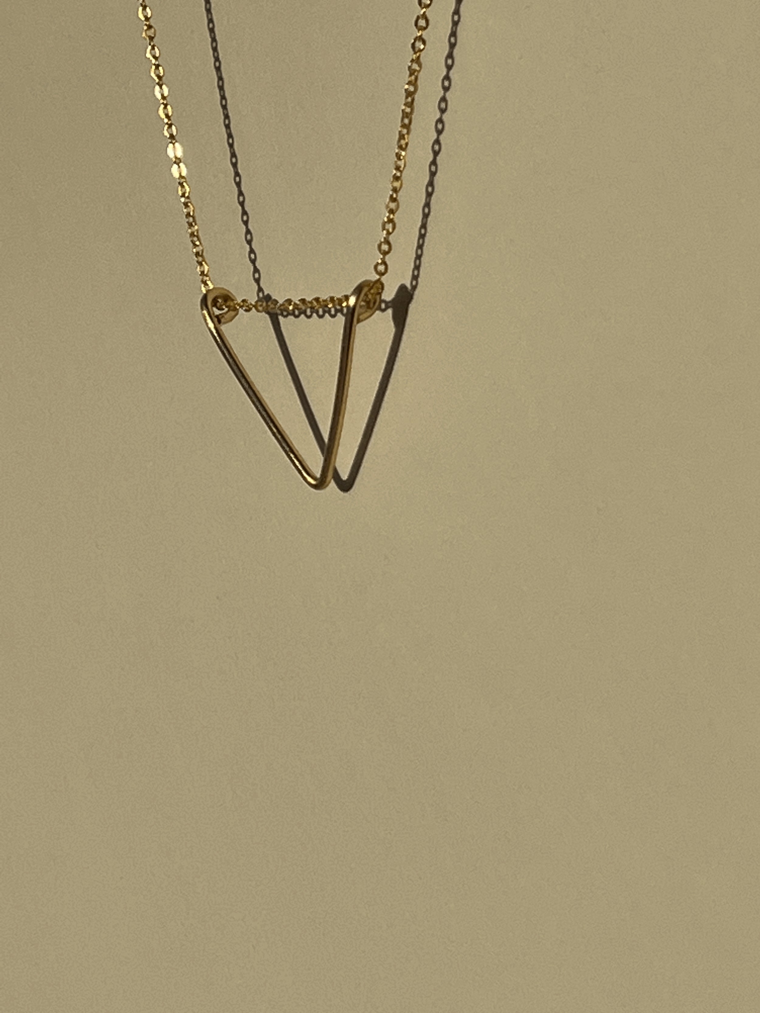 Side view of yellow gold-filled V pendant necklace suspended in air with shadows on a neutral background