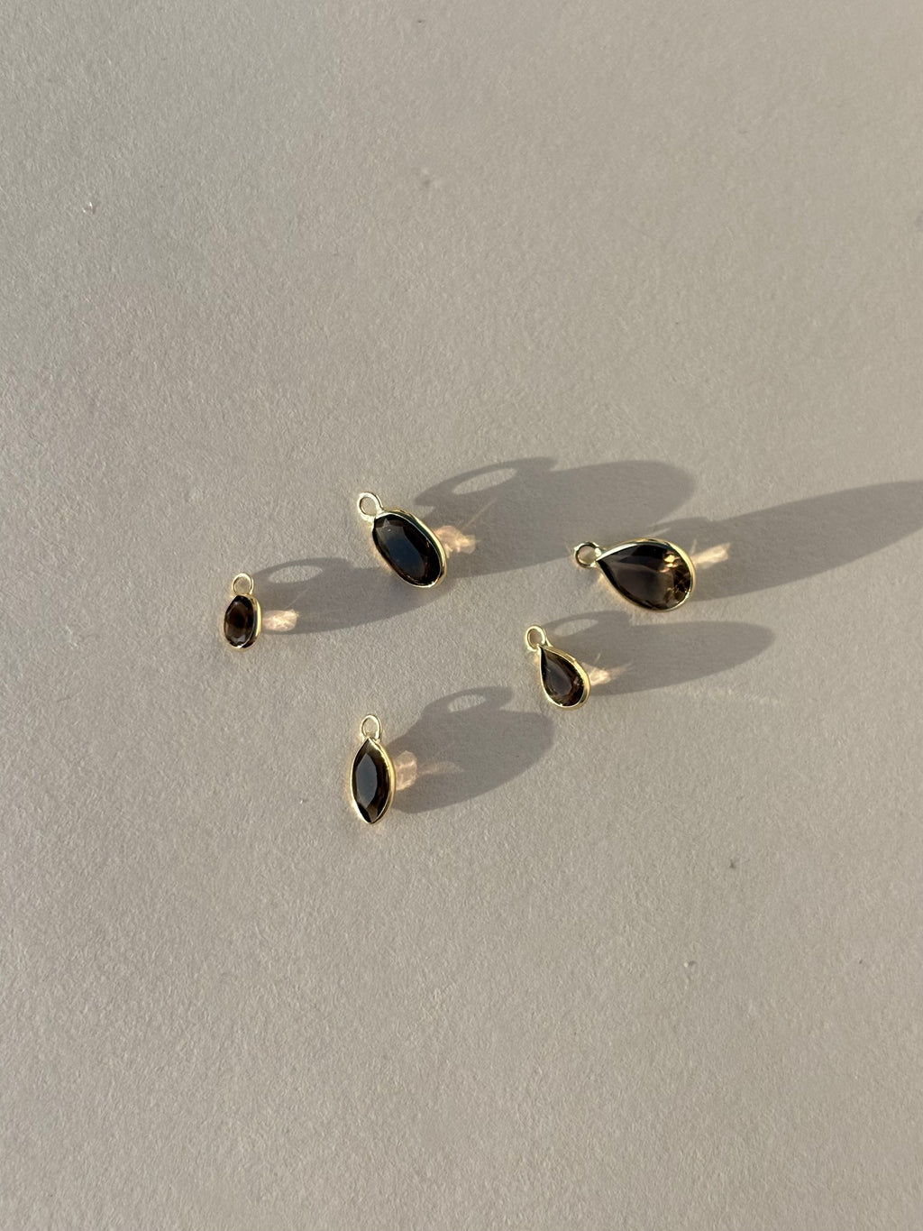 Collection of Thalken 14k solid gold single drop earring charms in natural smoky quartz, featuring pear, marquise, and oval shapes, displayed unattached to hoops for customizable styling