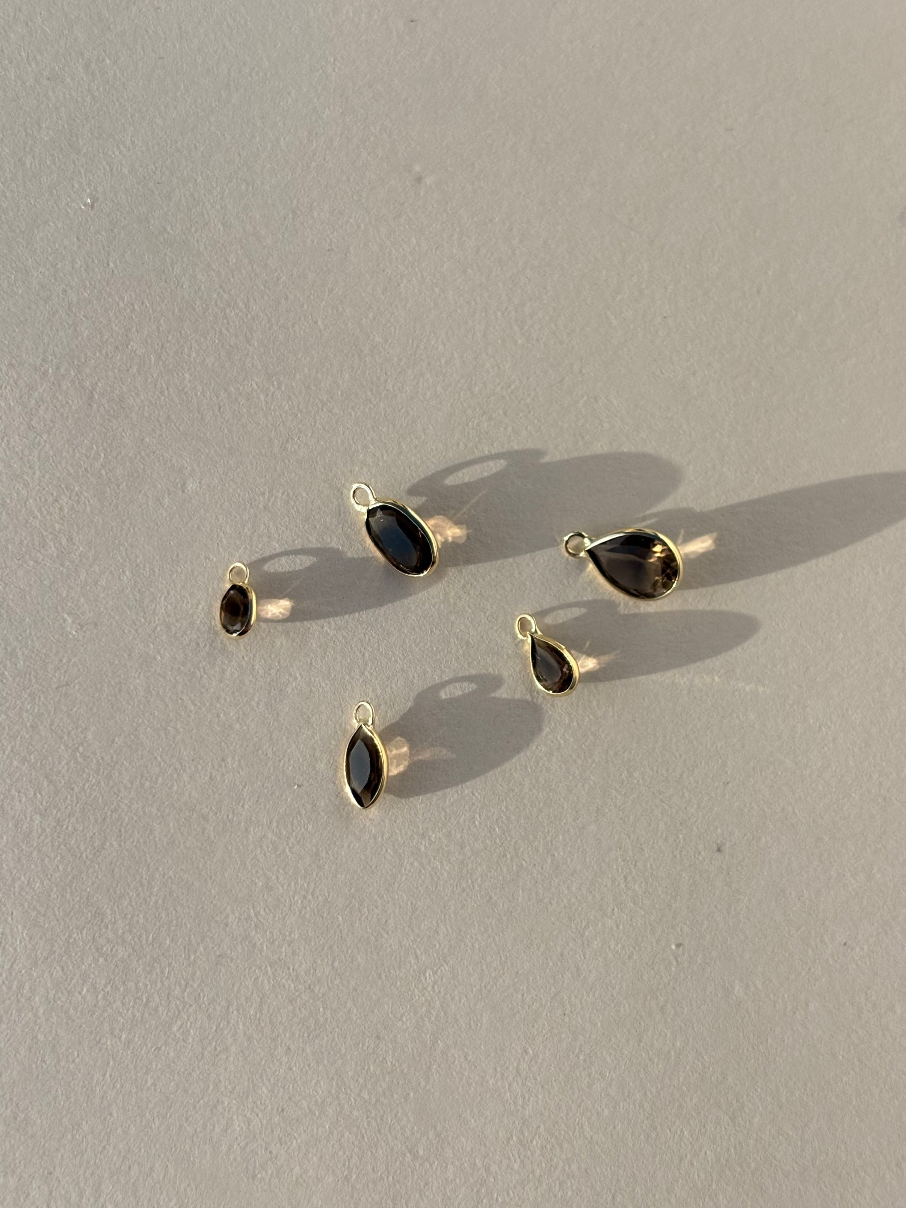 Collection of Thalken 14k solid gold single drop earring charms in natural smoky quartz, featuring pear, marquise, and oval shapes, displayed unattached to hoops for customizable styling