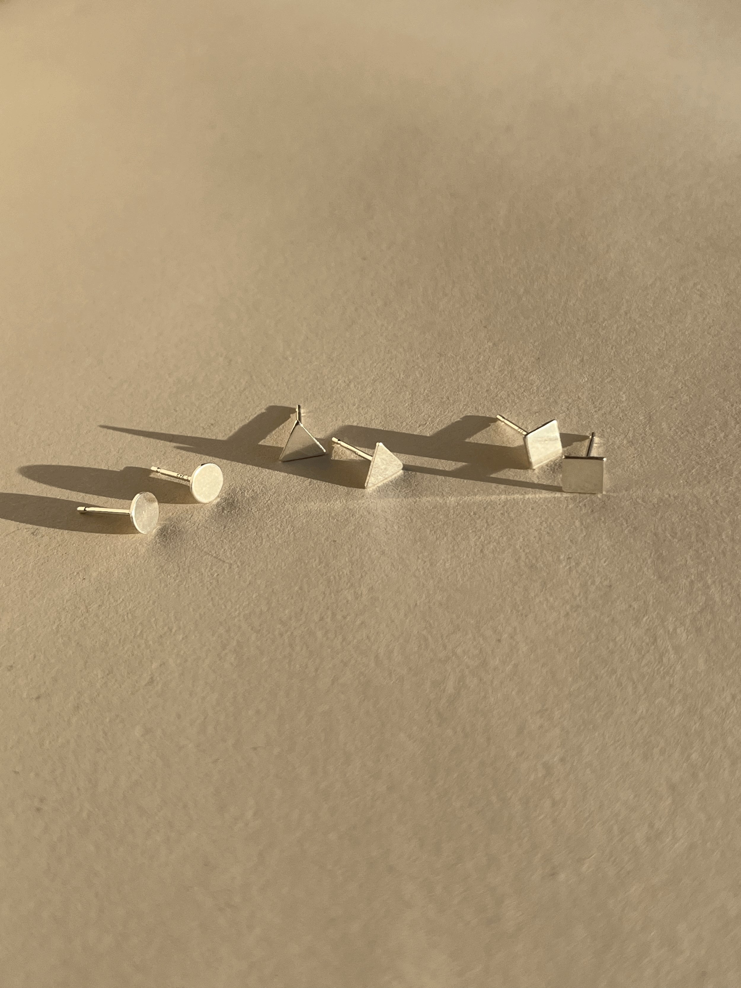 Pair of sterling silver square studs, pair of sterling silver triangle studs, and pair of sterling silver circle studs displayed on a neutral background.