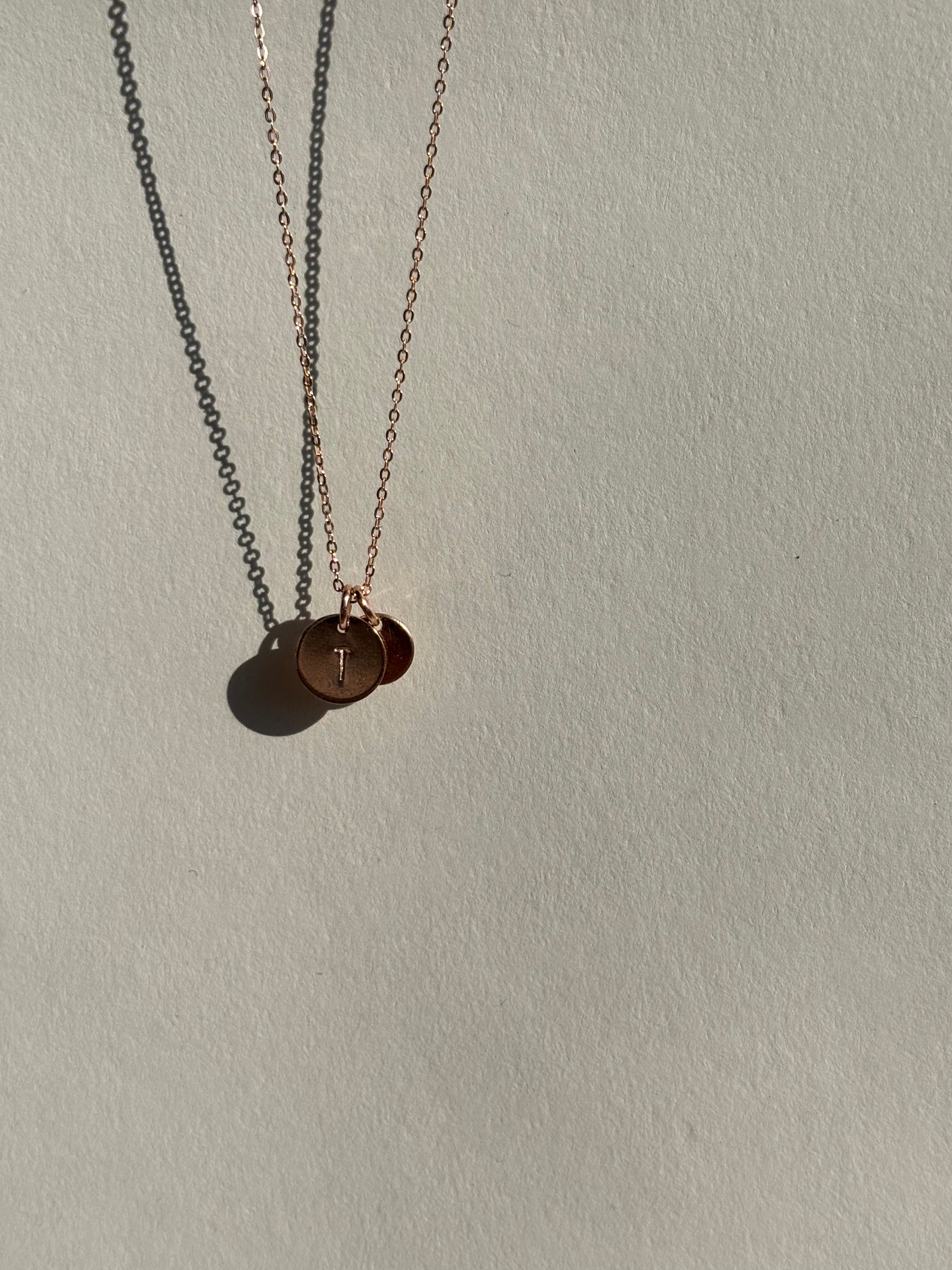 Rose gold-filled 9mm disc charm with an uppercase “T” in front, with a 7mm “H” charm layered behind