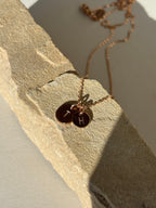 Rose gold-filled 7mm and 9mm stamped letter disc charms with “H” and “T” laying on a natural rock surface
