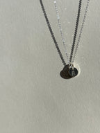 Alternate angle of a sterling silver 7mm “B” disc charm in front of a 9mm “H” disc charm on a chain