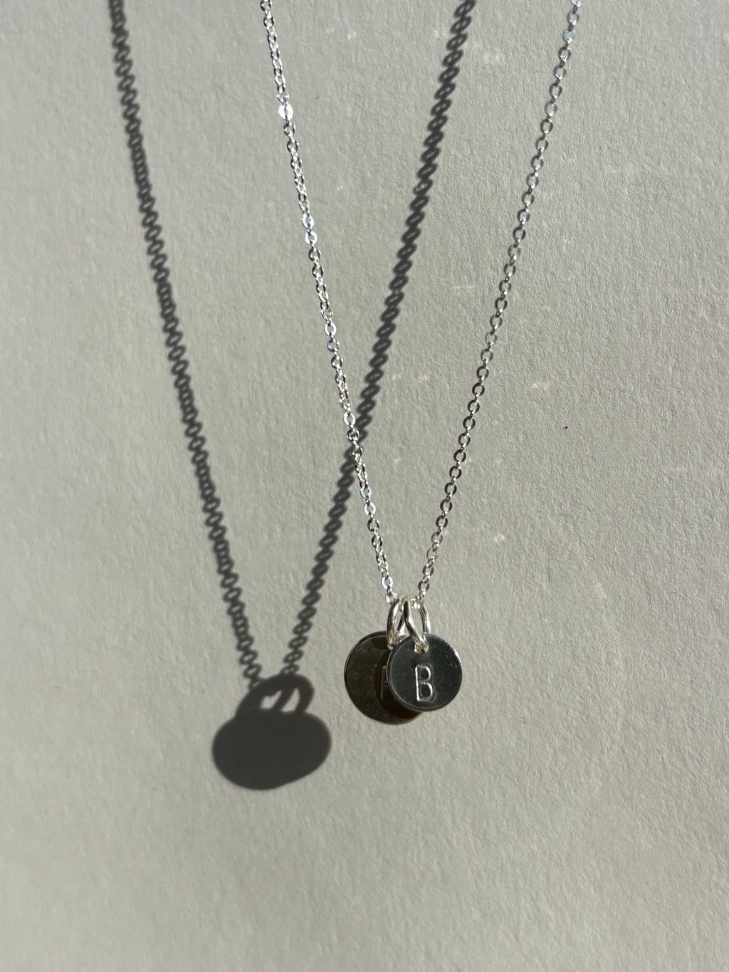 Sterling silver 7mm disc charm stamped with “B” layered in front of a 9mm “H” disc charm on a chain