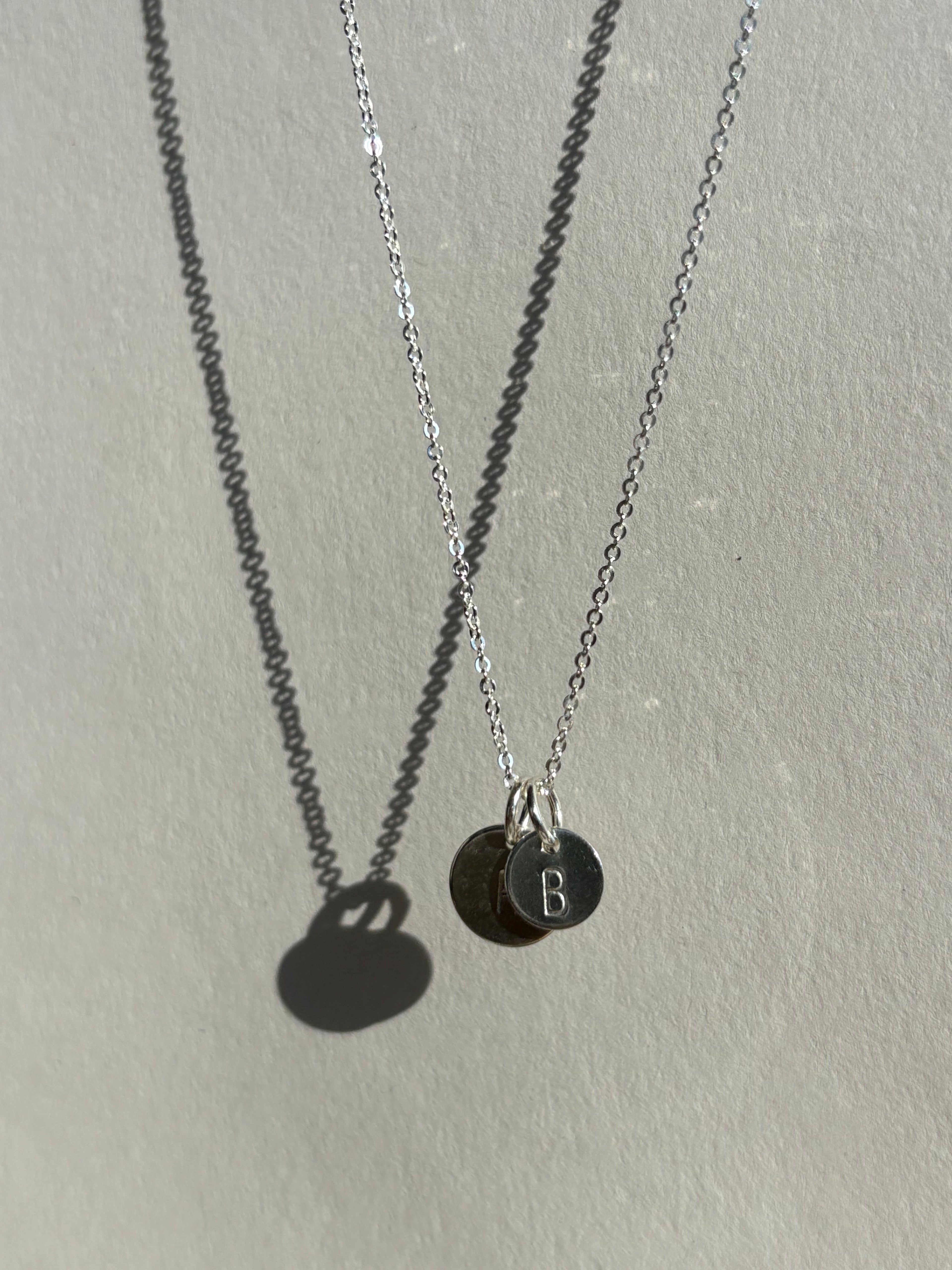 Sterling silver 7mm disc charm stamped with “B” layered in front of a 9mm “H” disc charm on a chain