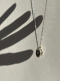 Sterling silver necklace with a 9mm disc charm stamped with “H” layered in front of a 7mm “B” disc, with a hand shadow appearing to touch the charms