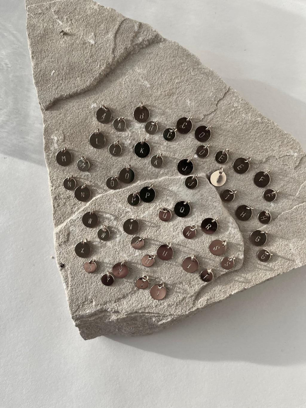 All letters of the alphabet stamped on sterling silver disc charms in both 7mm and 9mm sizes, displayed together on a light background