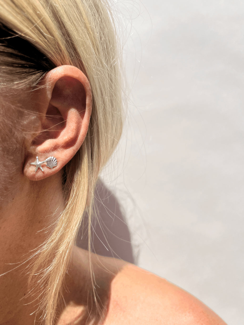 Model wearing skinny sterling silver starfish stud in first ear piercing and tiny shell stud in second