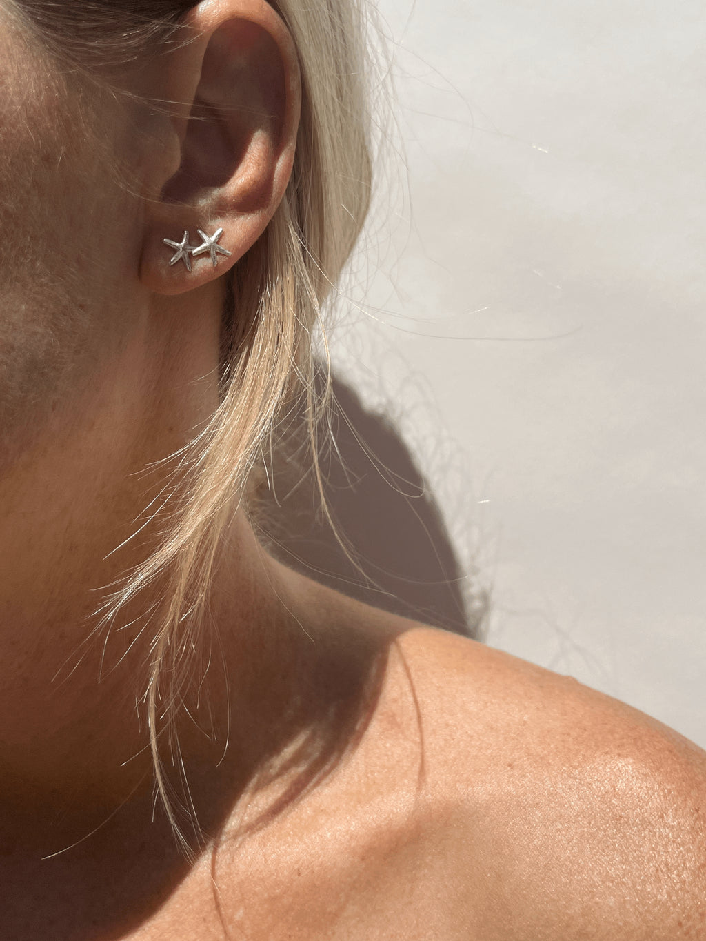 Model wearing skinny sterling silver starfish studs in both first and second ear piercings