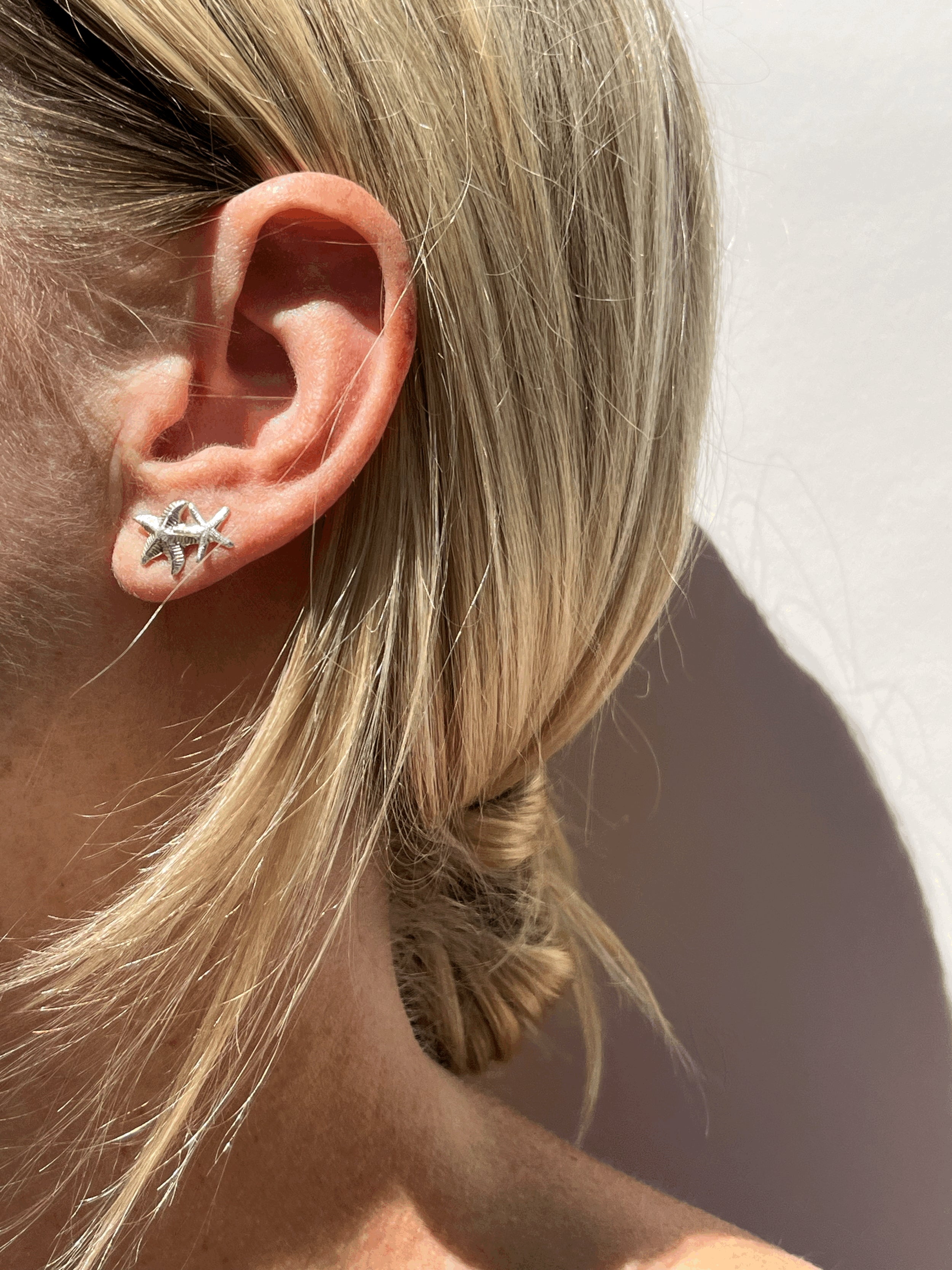 Model wearing thick sterling silver starfish stud in first ear piercing and skinny starfish stud in second