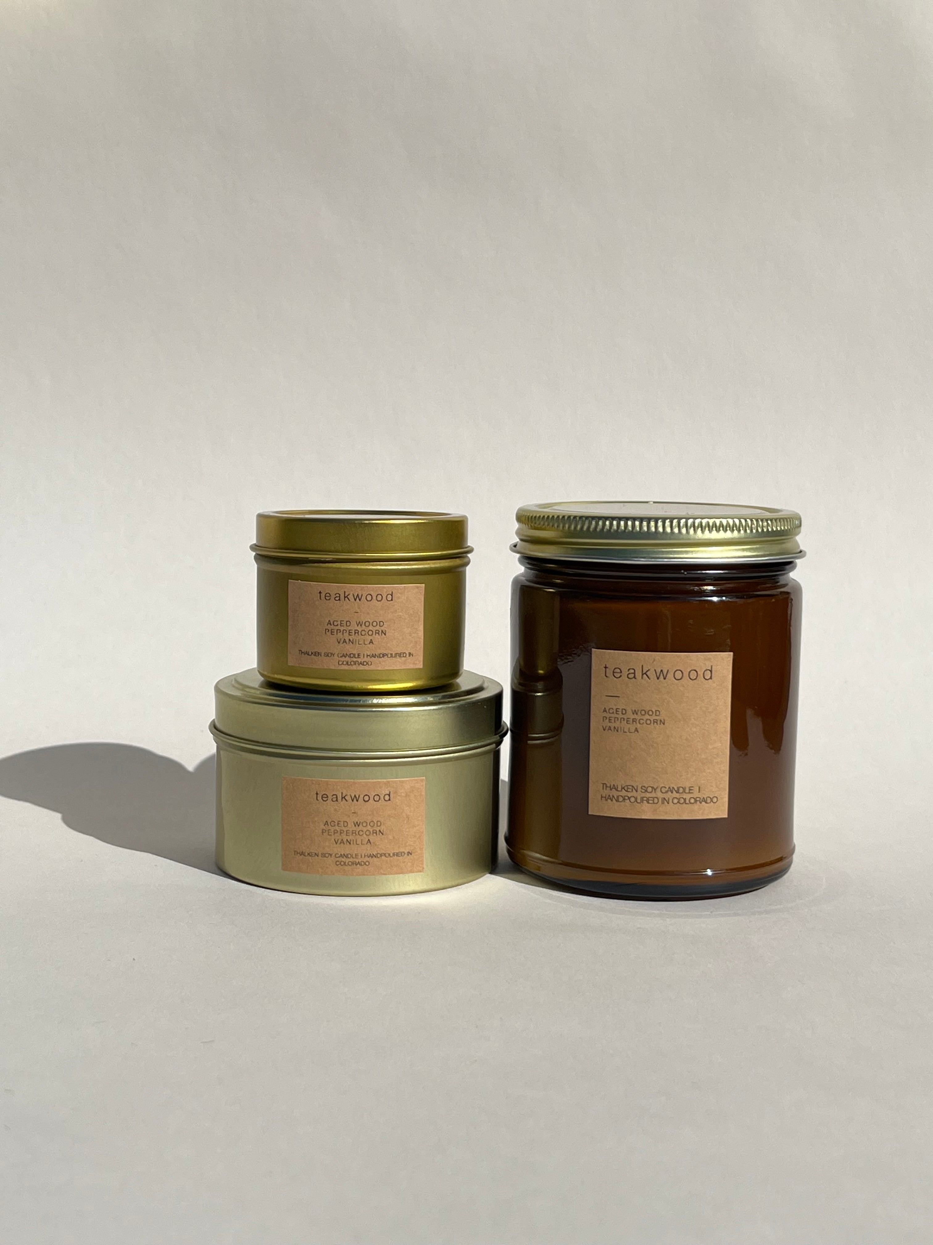 Thalken Teakwood Candle in three sizes — small gold tin, medium gold tin, and large brown glass jar — earthy and grounding with notes of aged teakwood, tobacco leaf, and a hint of peppercorn