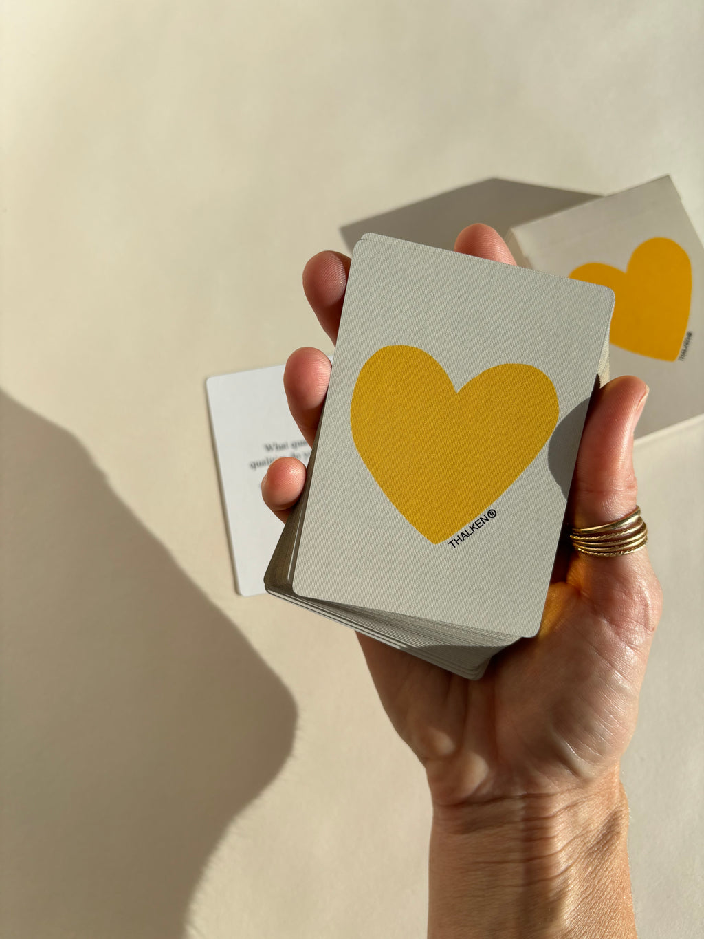 Hand holding a Thalken Heart Questions deck with a large yellow heart on the front and gold-gilded edging, glowing in warm light