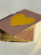 Thalken Heart Questions Volume 2 deck fanned out in warm light, showcasing the gold edging and dusty rose tones