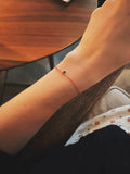 Close-up of the Thalken I AM bracelet on a wrist, glowing under warm restaurant lighting, featuring a thin red cord