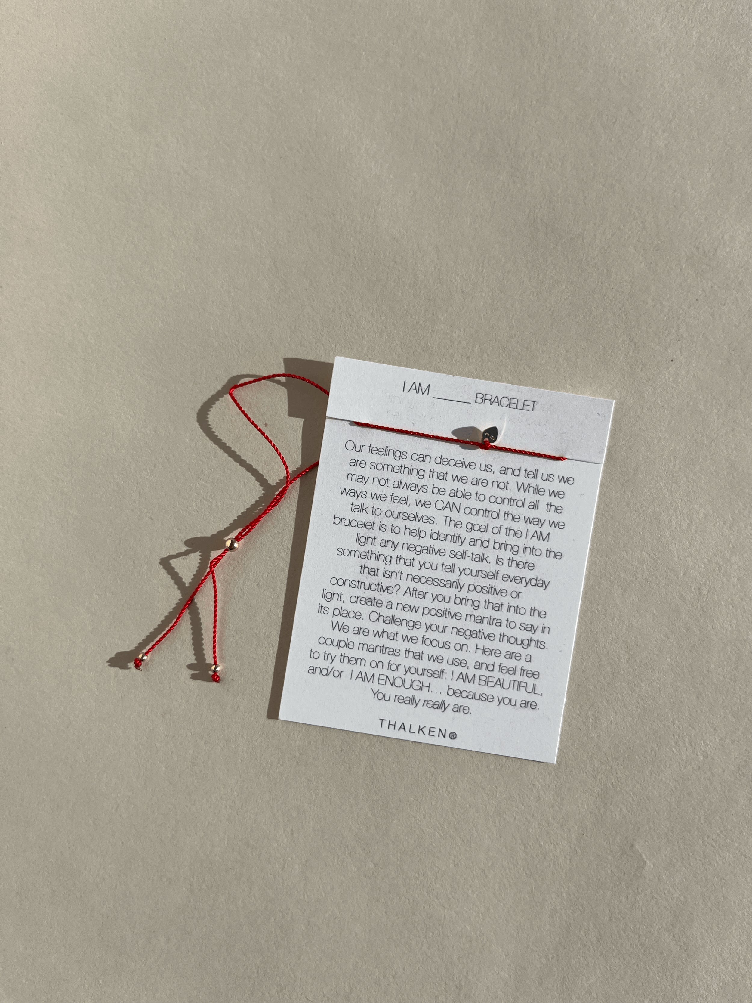 'I Am' bracelet with red cord on mantra card, styled against a neutral flat-lay background