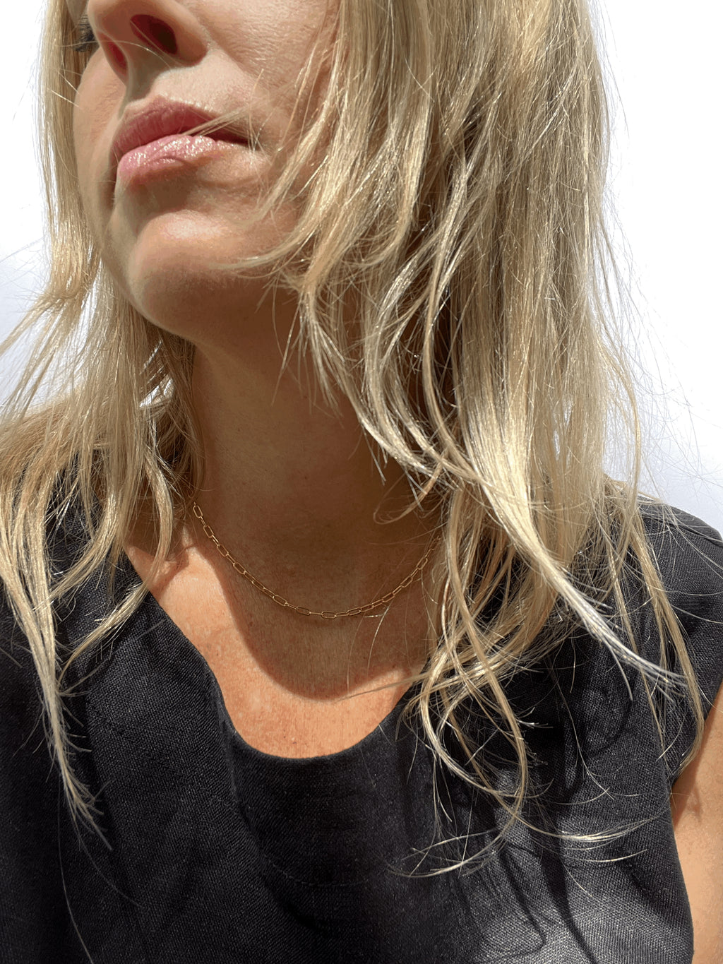 Model with blond hair wearing the rose gold-filled small link paperclip necklace with a black linen top