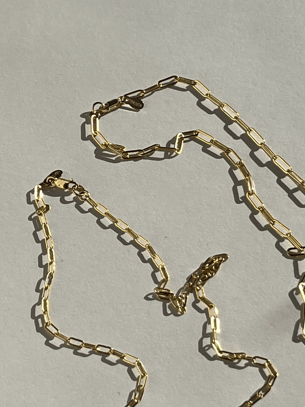 Yellow gold-filled small and medium link paperclip necklaces laying on a neutral surface