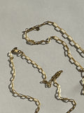 Yellow gold-filled small and medium link paperclip necklaces laying on a neutral surface