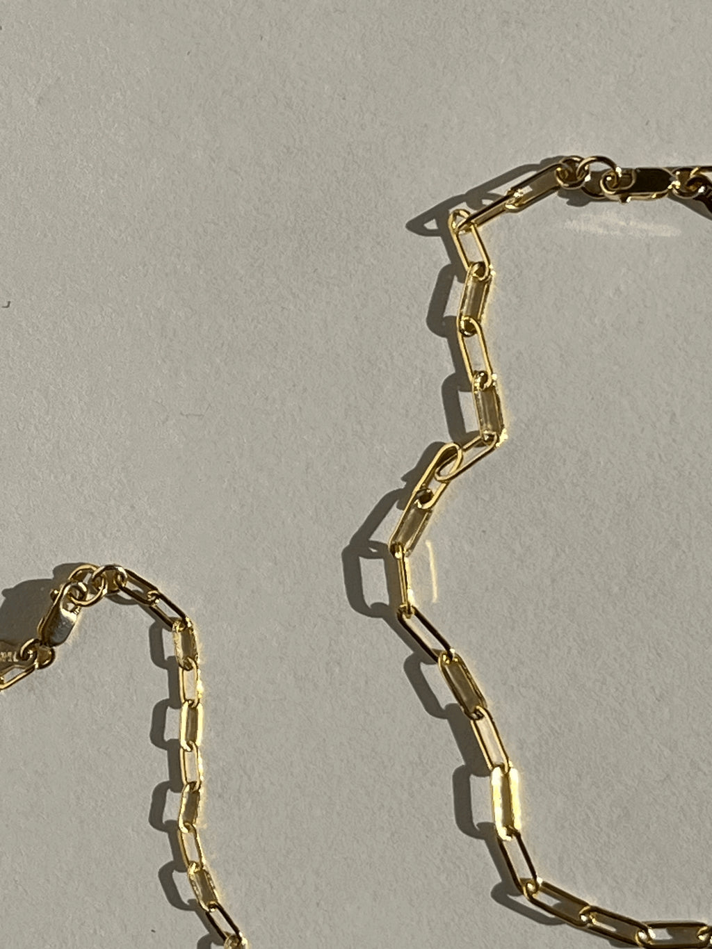 Close-up detail of yellow gold-filled small and medium link paperclip necklaces on a neutral surface