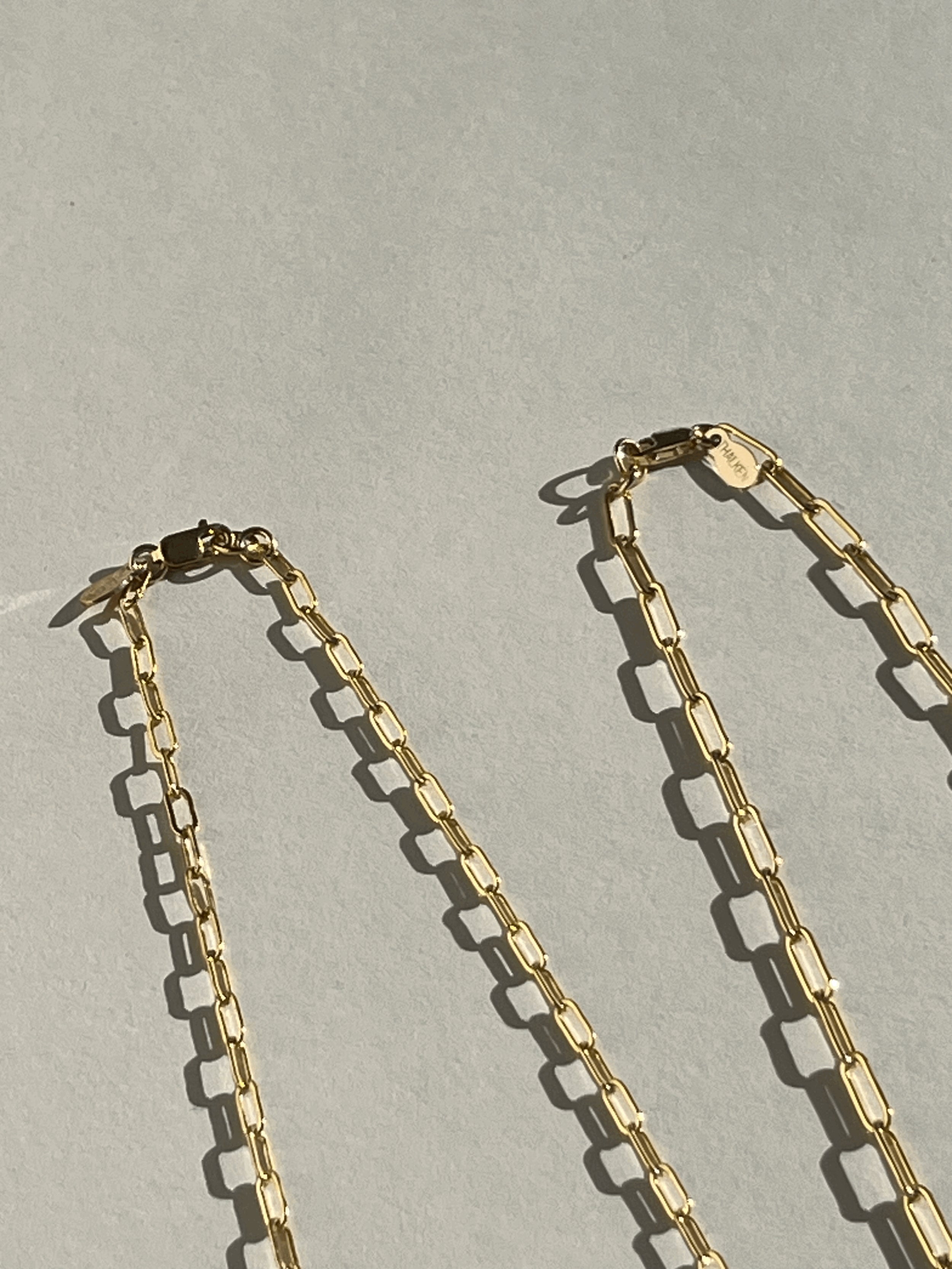Yellow gold-filled small and medium link paperclip necklaces laid out straight on a neutral backdrop
