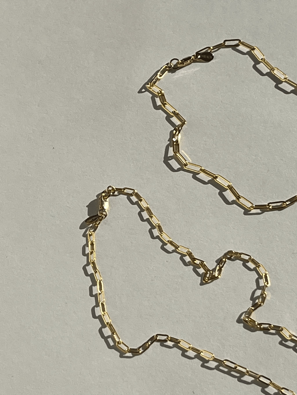 Yellow gold-filled small and medium link paperclip necklaces laying on a neutral surface