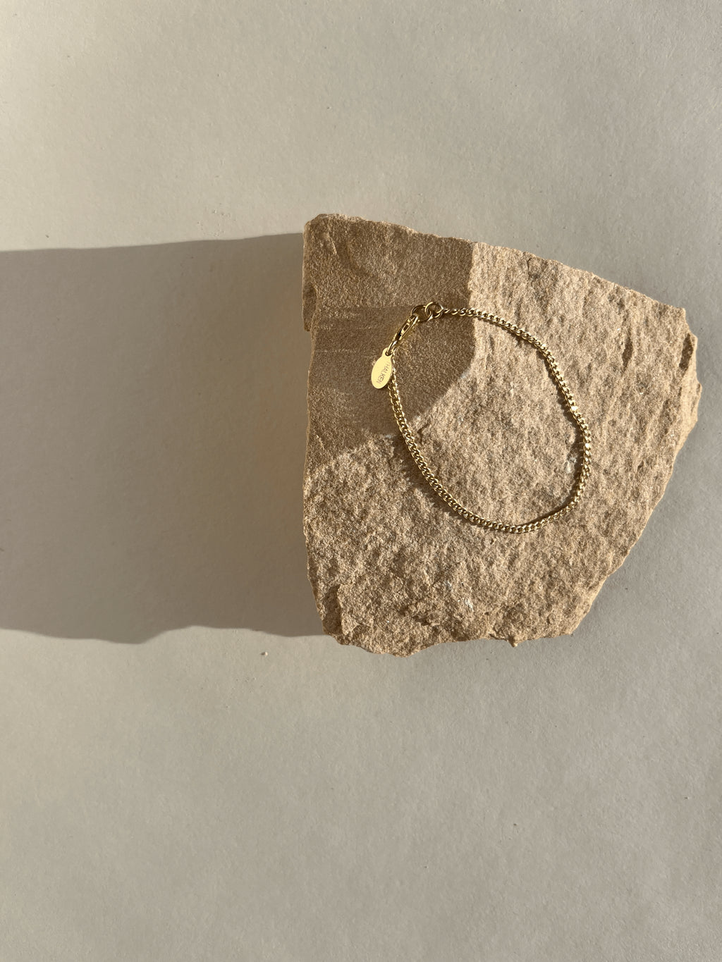 Thalken Perfect Curb Chain Bracelet in yellow gold-filled displayed on a rock in warm light at an angle