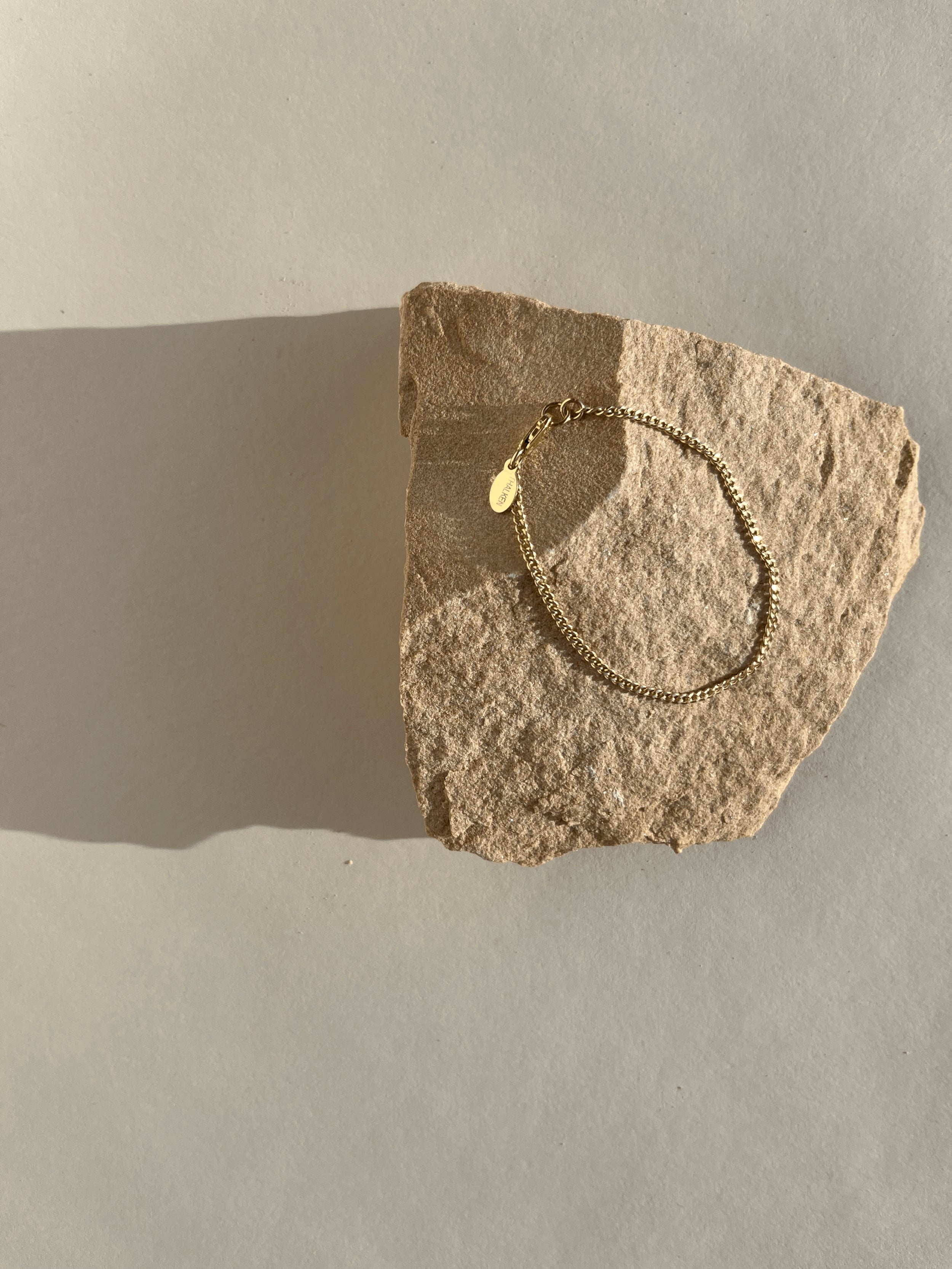 Thalken Perfect Curb Chain Bracelet in yellow gold-filled displayed on a rock in warm light at an angle