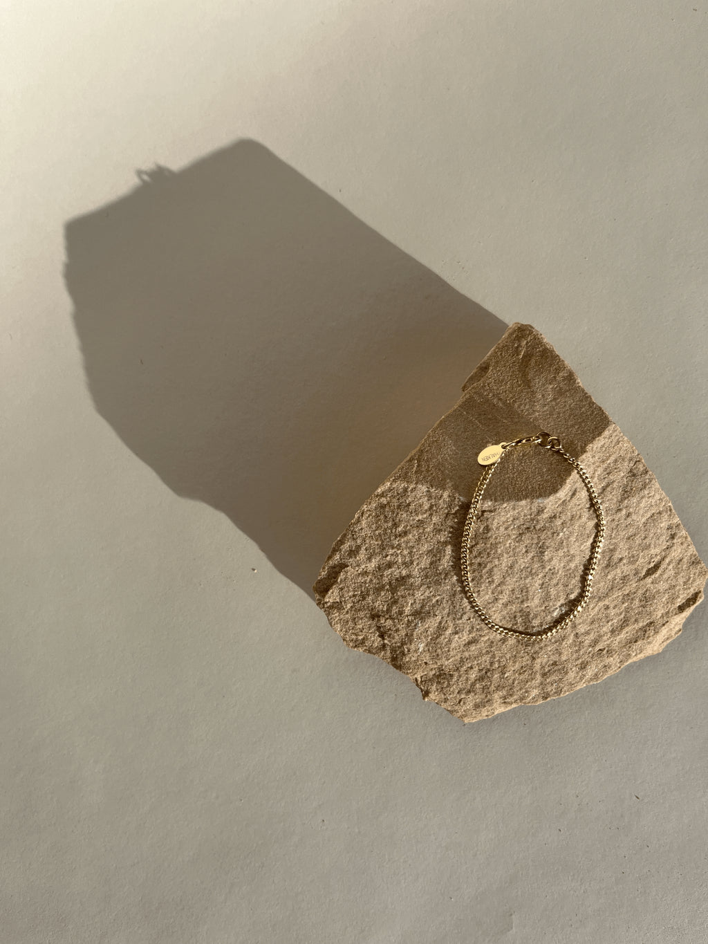 Thalken Perfect Curb Chain Bracelet in Yellow Gold-filled displayed on a rock in warm light, straight on