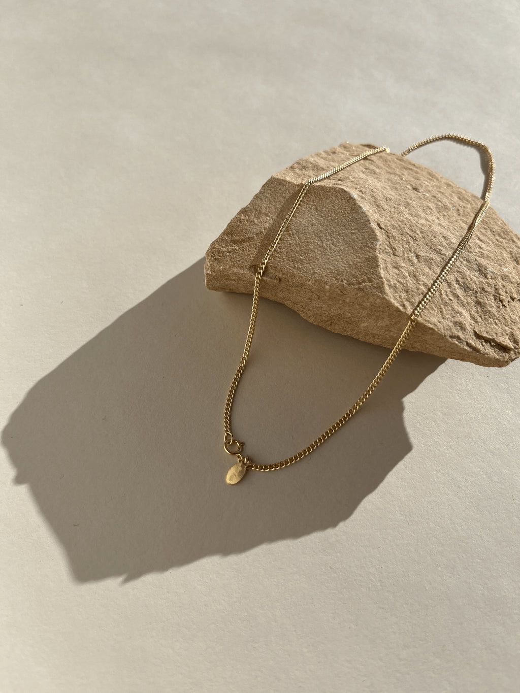 Minimalist necklace draped over a textured rock, glowing in bright, warm natural light