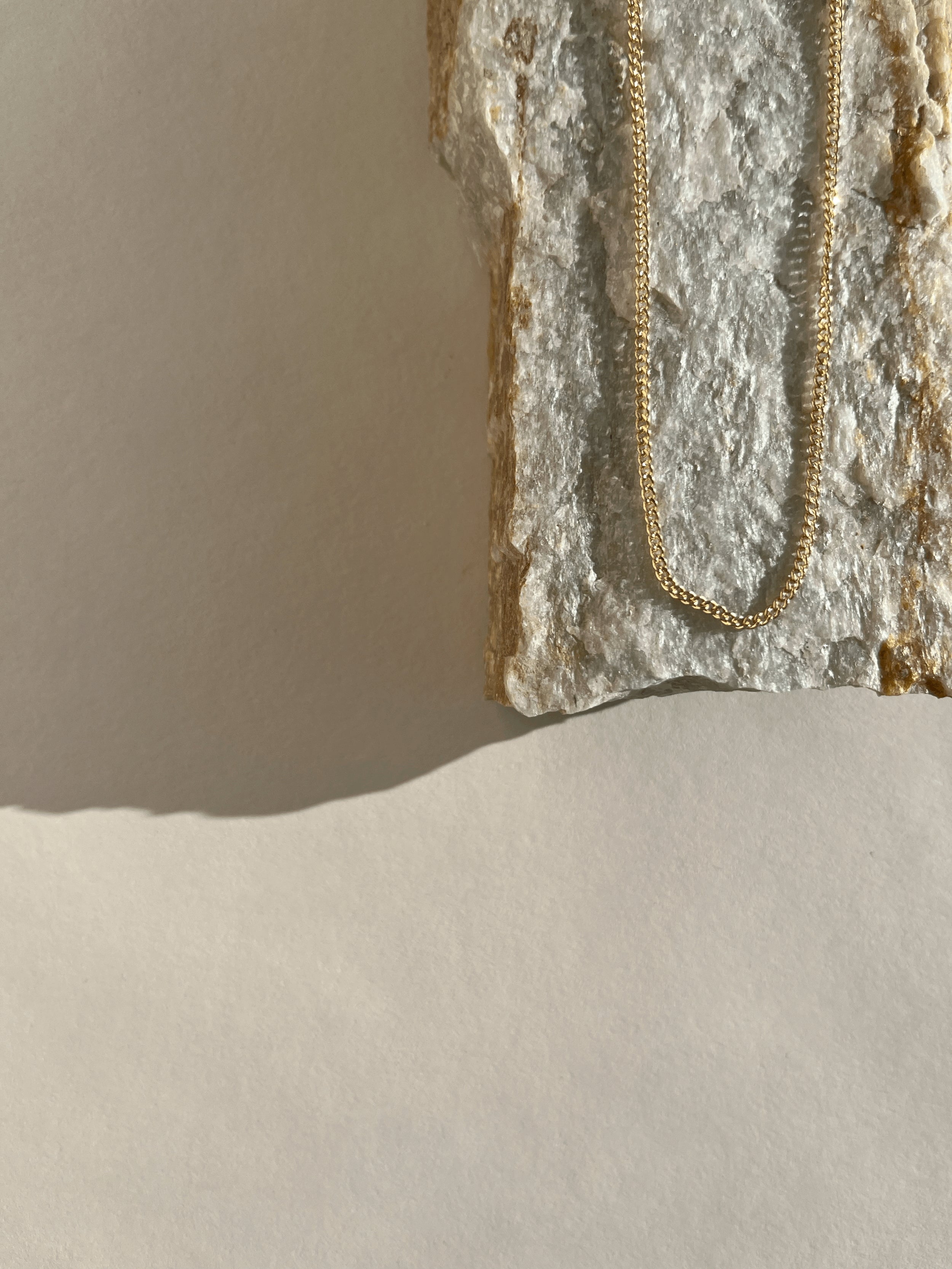 Necklace displayed on a natural organic rock, highlighting the warm glow of the yellow gold-filled chain