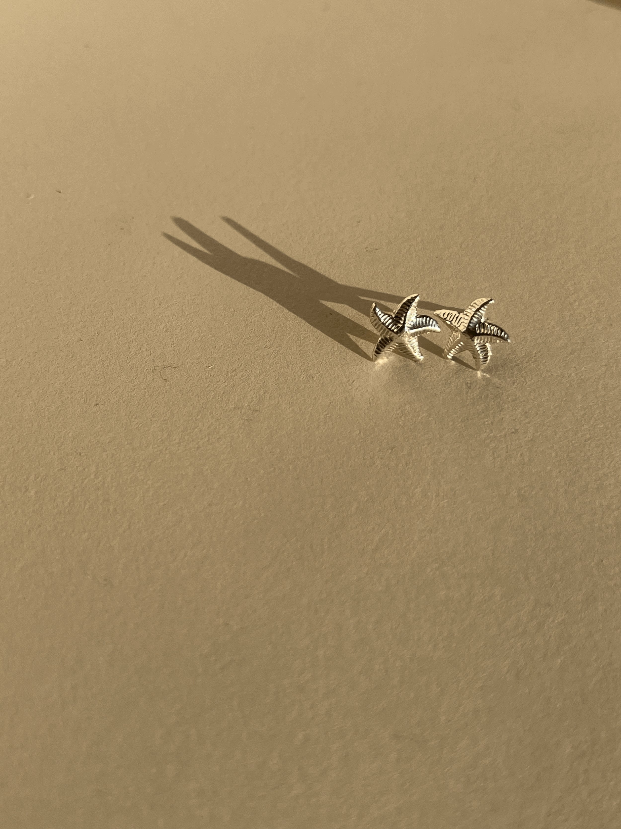Pair of thick sterling silver starfish stud earrings on a neutral background