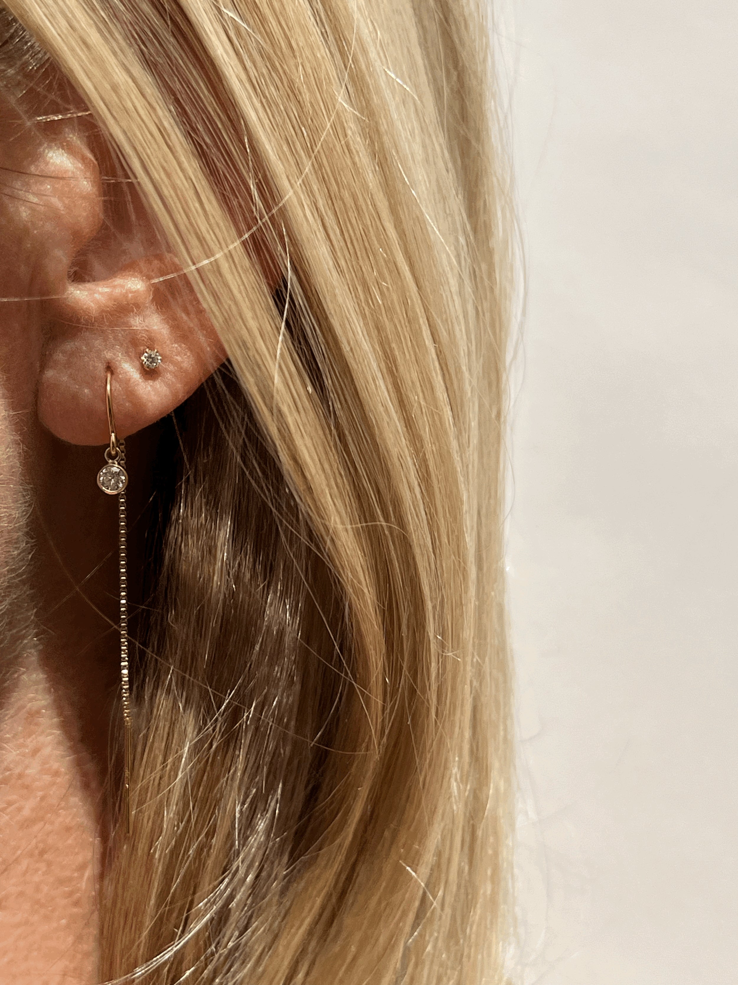 Model wearing Thalken’s yellow gold-filled clear cubic zirconia bezel threader earring in her first ear piercing, paired with clear Itty Bitty Crystal Studs in her second piercing, available in a separate listing