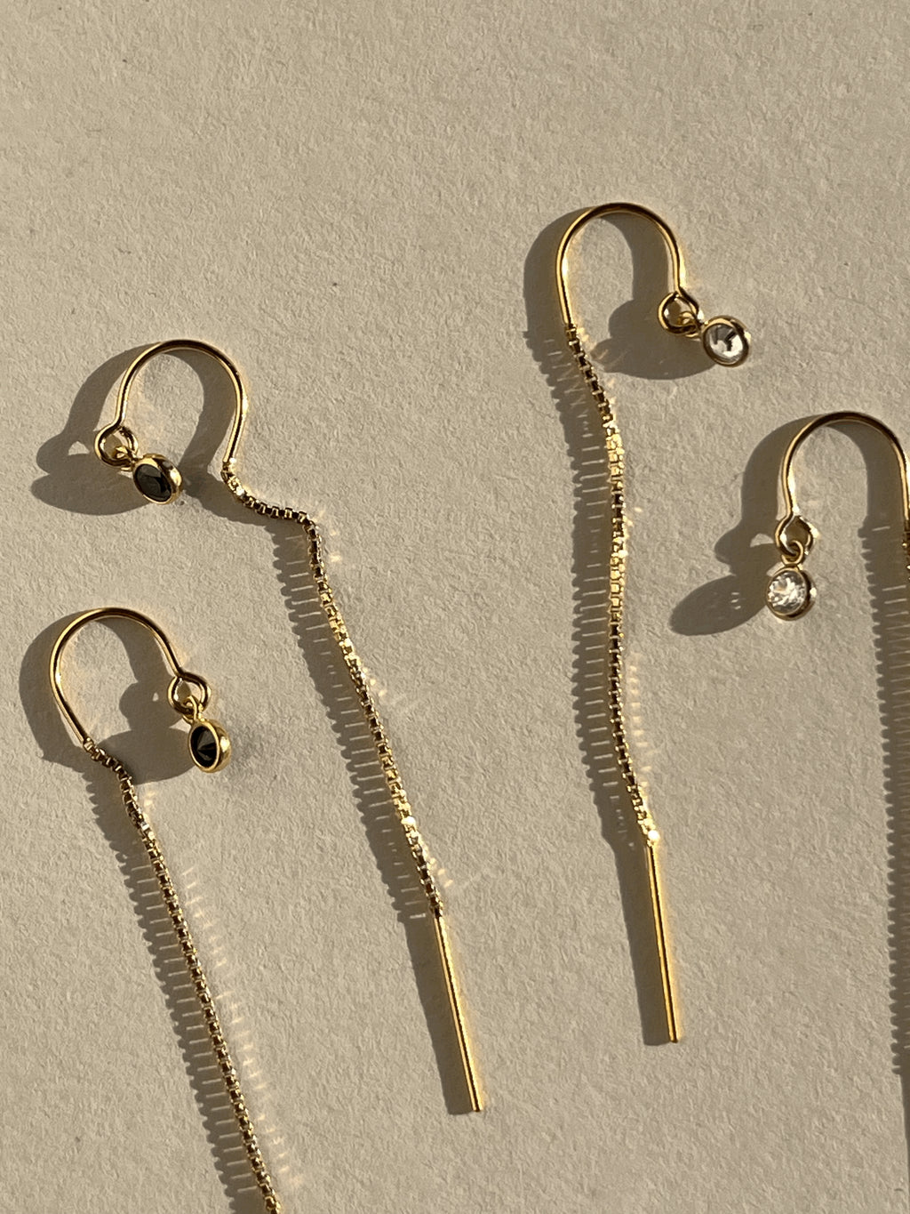 Flat-lay of Thalken’s yellow gold-filled CZ bezel threader earrings with clear and black cubic zirconia, styled for a minimalist aesthetic