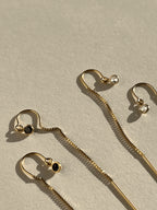 Close-up of wo pairs of Thalken’s yellow gold-filled CZ bezel threader earrings displayed on a neutral background, one with black cubic zirconia and one with clear cubic zirconia