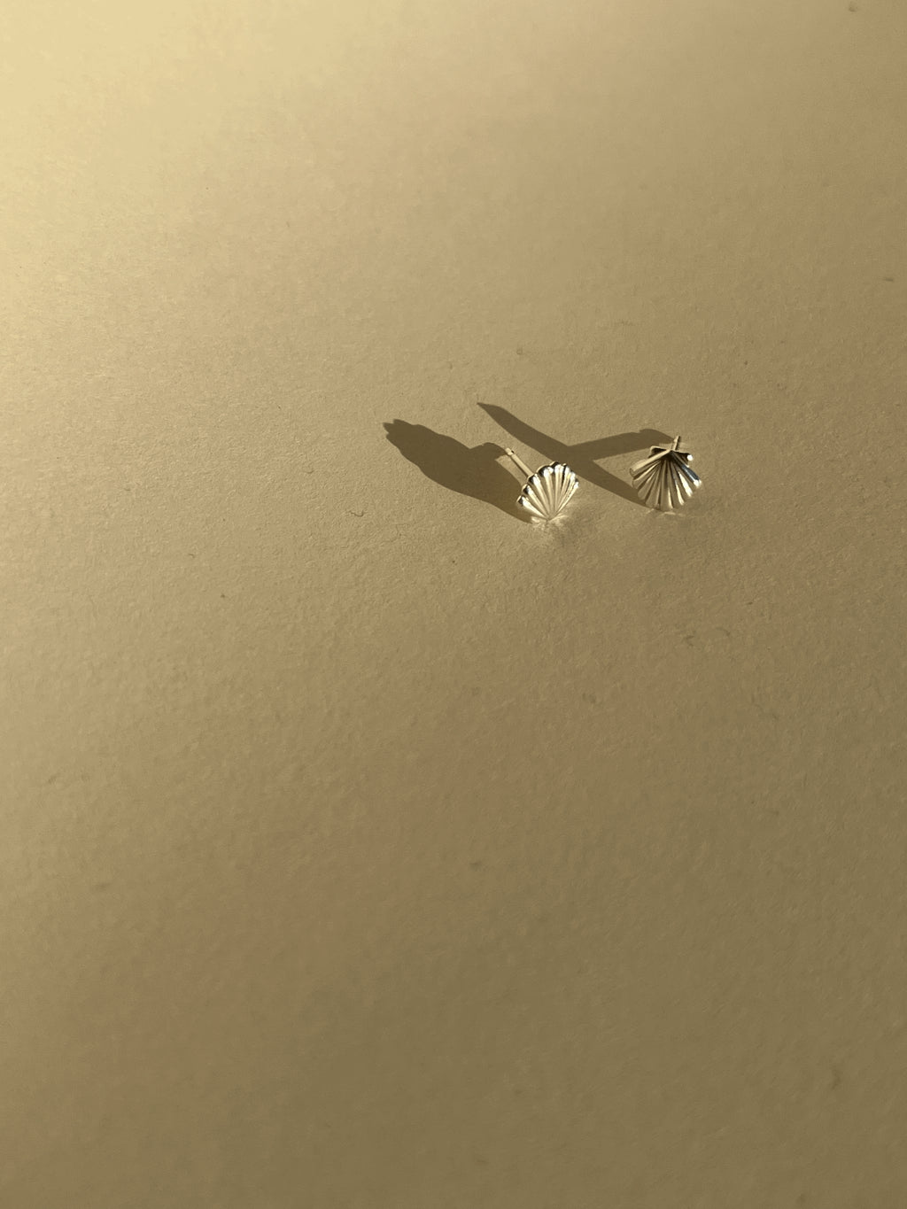 Pair of tiny sterling silver shell stud earrings on a neutral background
