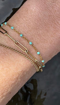 Close-up of model’s wrist in water wearing a yellow gold-filled bracelet stack featuring Thalken® Large Link Bracelet, turquoise enamel bead bracelet, and Perfect Curb Chain Bracelet